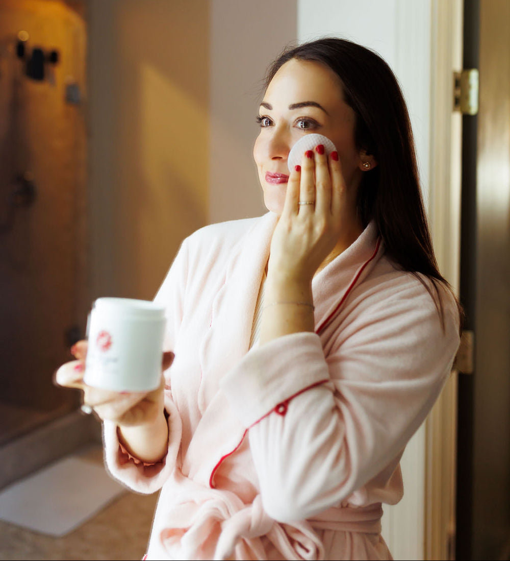 A woman in a pink robe is applying skincare in a bathroom